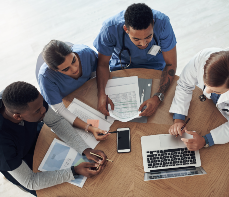 Top view of four people in blue scrubs looking at a laptop