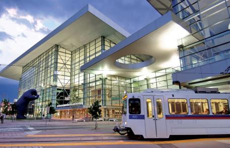 Street view of glass walled convention center, with a white bus driving in the foreground